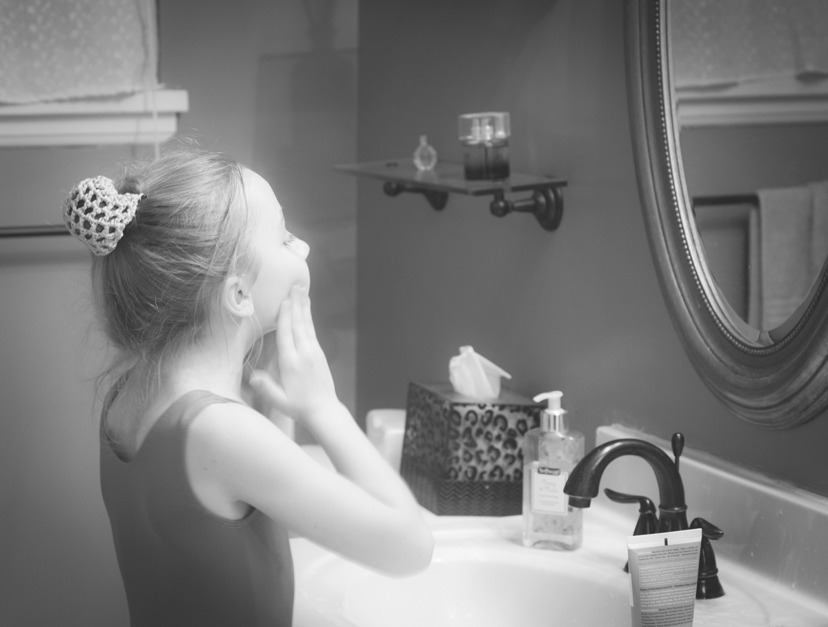 A young girl looks in the bathroom mirror as she washes her face. Not so SAHM