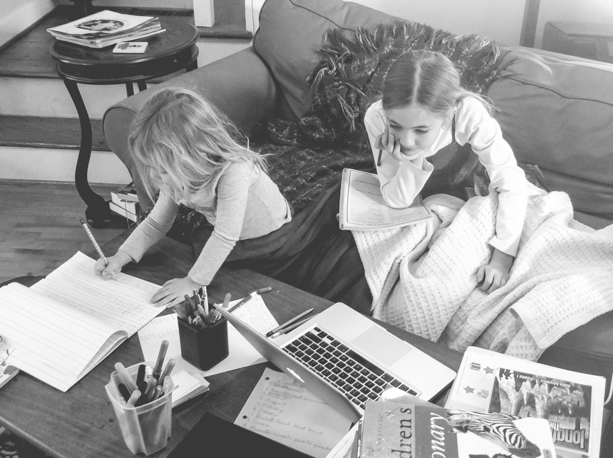 Two young girls sit on the couch to do homeschool work. Photo by Not So SAHM